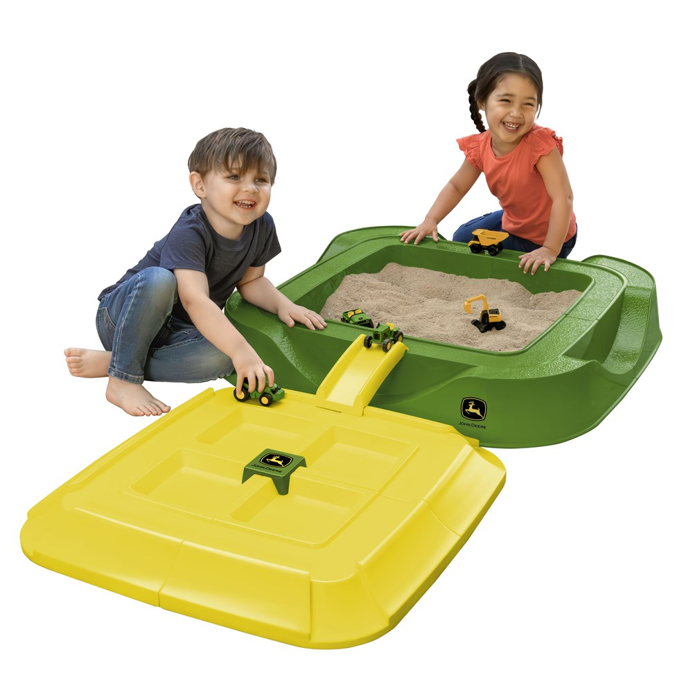 Two children playing with a green and yellow John Deere outdoor sand pit, lid and toy vehicles