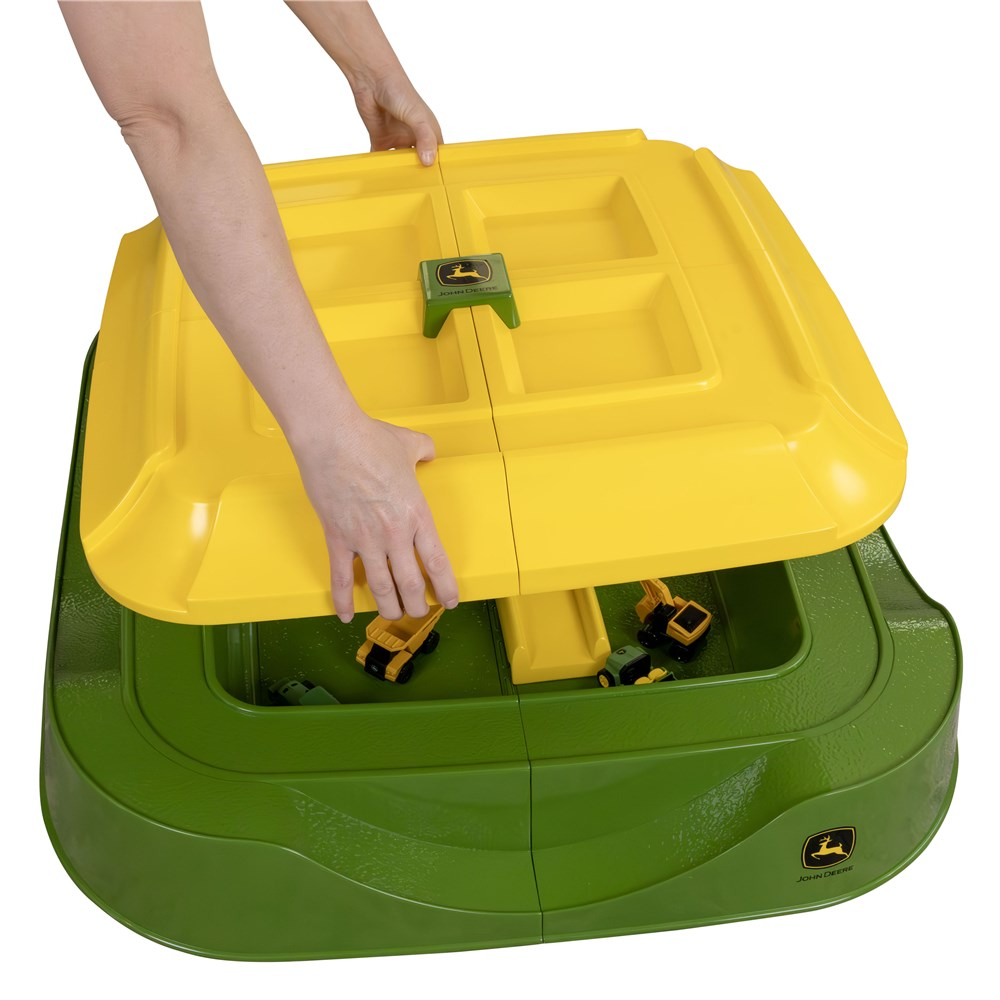 Yellow storage lid being fitted to the green John Deere sand pit with toy vehicles stored inside